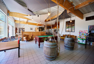 Sala giochi interna al Camping La Roche d’Ully con biliardo, calcetto, divanetti e giochi arcade in Francia.