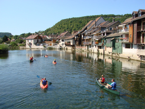 Persone in canoa su un fiume tranquillo accanto a case tradizionali in Bourgogne-Franche-Comté, Francia.