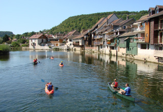 Folk padler i kanoer på en rolig flod forbi traditionelle huse i Bourgogne-Franche-Comté, Frankrig.