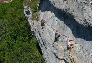 Three climbers with helmets scale a steep cliff face at Camping La Roche d’Ully in Bourgogne-Franche-Comté, France.