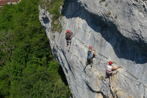 Three climbers with helmets scale a steep cliff face at Camping La Roche d’Ully in Bourgogne-Franche-Comté, France.