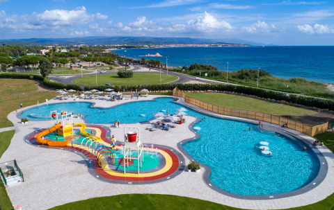 Vista aérea de Camping Laguna Blu en Cerdeña con piscina, toboganes acuáticos y fondo de mar azul.