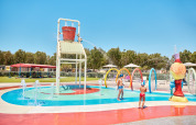 Børn leger under en stor vandskov i børnevenligt splash-område på Camping Laguna Blu i Sardinien.