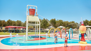 Children play under a large tipping bucket in the splash park at Camping Laguna Blu, Sardinia, Italy.