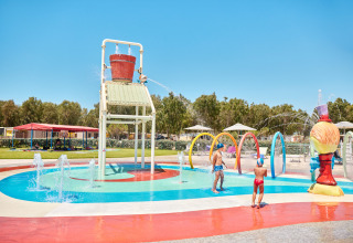 Kinder spielen im Wasserspielbereich mit großem Kippeimer auf dem Campingplatz Laguna Blu in Sardinien.