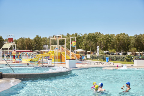 Niños juegan en el parque acuático de Camping Laguna Blu en Cerdeña, Italia, con toboganes y piscina.