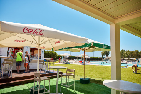 Ospiti si rilassano al bar della piscina sotto gli ombrelloni al Camping Laguna Blu, Sardegna, Italia.