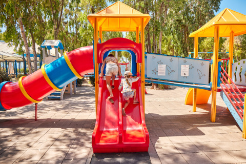 Niños jugando en un colorido parque infantil con toboganes en Camping Laguna Blu en Cerdeña, Italia.