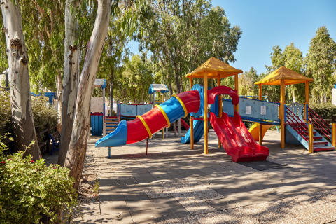 Área de juegos colorida con toboganes y estructuras bajo árboles en Camping Laguna Blu, Cerdeña, Italia.