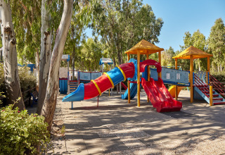 Kleurige speeltuin met glijbanen en klimtoestellen onder bomen bij Camping Laguna Blu, Sardinië, Italië.