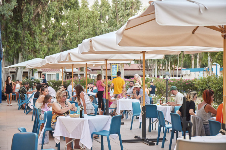 Außenbereich eines Restaurants im Camping Laguna Blu, Sardinien, Italien, mit Gästen unter Sonnenschirmen.