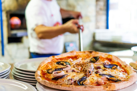 Versgebakken pizza met zeevruchten op borden in Camping Laguna Blu, een vakantiepark in Sardinië, Italië.