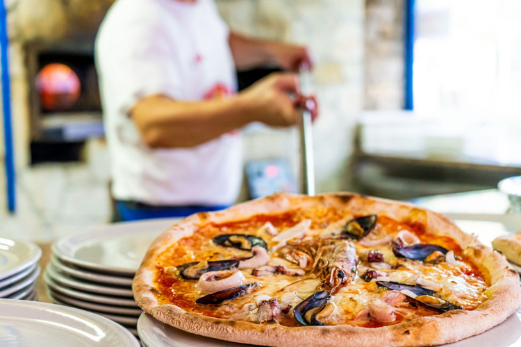 Frisch gebackene Meeresfrüchtepizza auf Tellern in der Ferienanlage Camping Laguna Blu auf Sardinien, Italien.