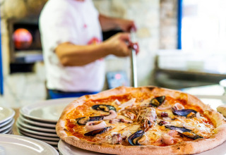 Friskbagt pizza med skaldyr serveres på tallerkener på Camping Laguna Blu, feriepark i Sardinien, Italien.