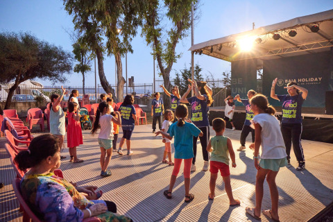 Niños y adultos participan en entretenimiento nocturno con baile grupal en Camping Laguna Blu, Cerdeña, Italia.