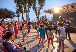 Kinderen en volwassenen genieten van avondanimatie met groepsdans op Camping Laguna Blu in Sardinië, Italië.