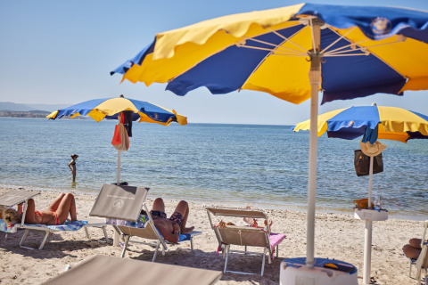 Spiaggia al Camping Laguna Blu, Sardegna, Italia, con lettini, ombrelloni e persone che si rilassano.