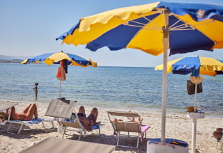 Spiaggia al Camping Laguna Blu, Sardegna, Italia, con lettini, ombrelloni e persone che si rilassano.