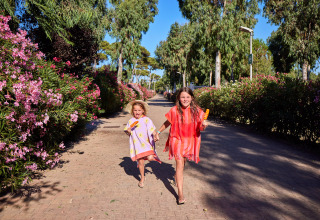 Two kids happily walking with ice lollies on a sunny path lined with flowers in Sardinia, Italy.