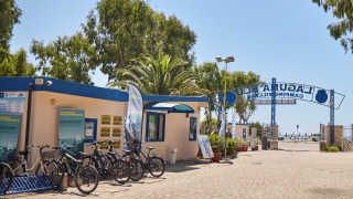 Entrance to Camping Laguna Blu in Sardinia, Italy, featuring a bike rental station and sunny beach access.