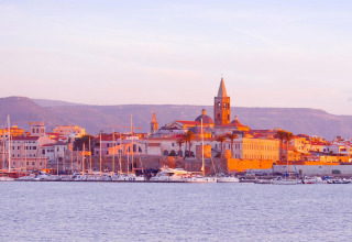 Både ved havnen i solnedgang på Camping Laguna Blu feriepark i Sardinien, Italien, med gamle bygninger i baggrunden.