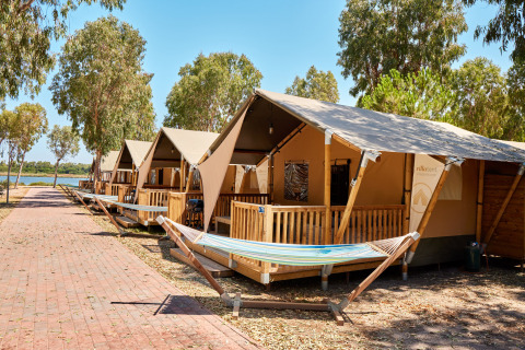 Filas de tiendas glamping con hamacas en Camping Laguna Blu en Cerdeña, Italia, cerca de árboles y sendero.