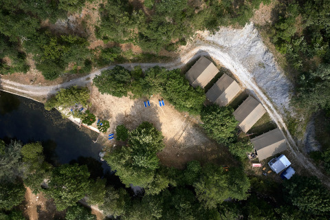 Aerial view of Camping Le Canigou in Occitanie, France, featuring tents, trees, and a nearby pond.