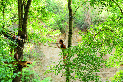 Twee mensen steken een avontuurlijk touwenparcours over tussen bomen bij Camping Le Canigou in Occitanië, Frankrijk.