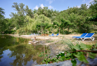 Relaxing lakeside with blue sun loungers and lush greenery at Camping Le Canigou, Occitanie, France.