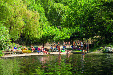 Holiday park guests relax and swim by a lake surrounded by lush trees at Camping Le Canigou in Occitanie, France.