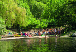 Feriepark gæster nyder solen og bader i søen blandt grønne træer på Camping Le Canigou i Occitanie, Frankrig.
