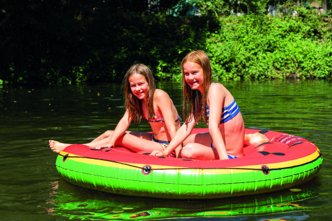 Two girls in swimsuits enjoying a sunny day on a colorful inflatable float at Camping Le Canigou, Occitanie, France.