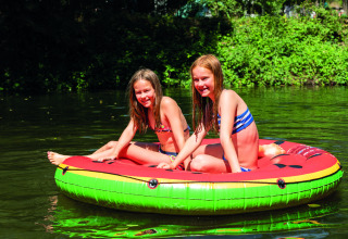 Due ragazze in costume si divertono su un gonfiabile colorato sull'acqua al Camping Le Canigou, Occitanie, Francia.