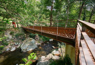 Ponte pedonale sul ruscello a Camping Le Canigou, Occitania, Francia, immerso nel verde.
