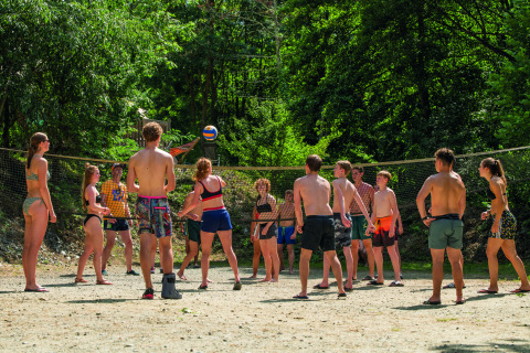 Jóvenes juegan voleibol al aire libre en Camping Le Canigou, rodeados de árboles verdes, en Occitanie, Francia.