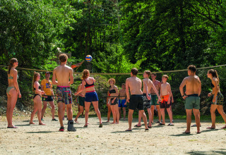 Teens play volleyball outdoors at Camping Le Canigou, surrounded by lush trees and summer sun in Occitanie, France.