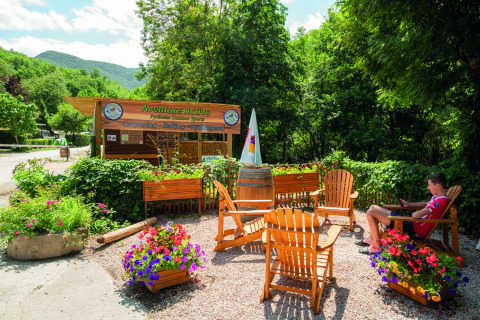 Area esterna con sedie di legno e fiori presso Aventure Active al Camping Le Canigou, Occitanie, Francia.