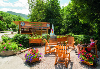 Area esterna con sedie di legno e fiori presso Aventure Active al Camping Le Canigou, Occitanie, Francia.