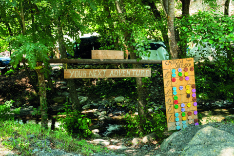 Área exterior en Camping Le Canigou, Francia, con cartel de aventura y tablero de actividades colorido.