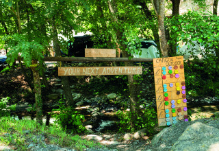 Outdoor area at Camping Le Canigou, France, with adventure sign and colorful activity schedule board.