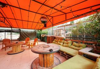 Outdoor lounge at Camping Le Canigou, Occitanie, France with orange canopy, cable spool tables, and cushions.