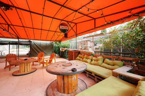 Buitenlounge bij Camping Le Canigou, Occitanië, Frankrijk, met oranje zeil, houten tafels en gezellige banken.