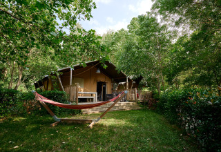 Safari tent with hammock and wooden deck surrounded by greenery at Camping Le Canigou, Occitanie, France.