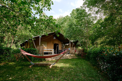 Safari tent with hammock and wooden deck surrounded by greenery at Camping Le Canigou, Occitanie, France.