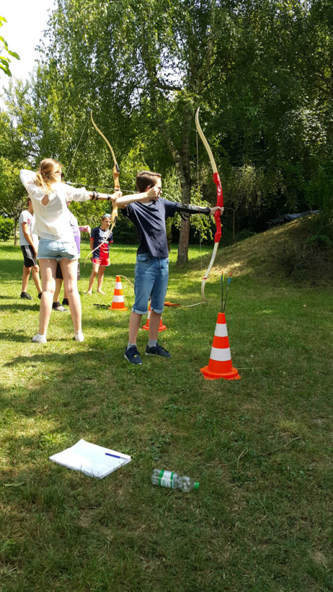 Adolescentes practican tiro con arco al aire libre en Camping Le Coin Tranquille, Auvergne-Rhône-Alpes, Francia.