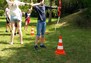 Teenagere deltager i bueskydning udendørs ved Camping Le Coin Tranquille i Auvergne-Rhône-Alpes, Frankrig.