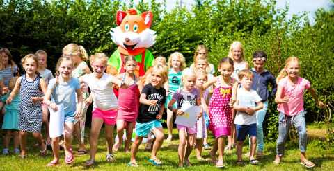 Bambini giocano all'aperto con una grande mascotte di volpe al Camping Le Coin Tranquille in Alvernia-Rodano-Alpi, Francia.