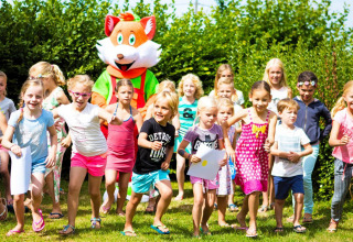 Børn leger udenfor med en stor ræv maskot på Camping Le Coin Tranquille i Auvergne-Rhône-Alpes, Frankrig.