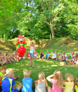 Børn leger i en cirkel udendørs i solskin ved Camping Le Coin Tranquille i Auvergne-Rhône-Alpes, Frankrig.