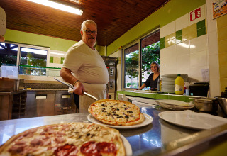 Uno chef serve una pizza appena sfornata nella cucina di Camping Le Coin Tranquille in Auvergne-Rhône-Alpes, Francia.